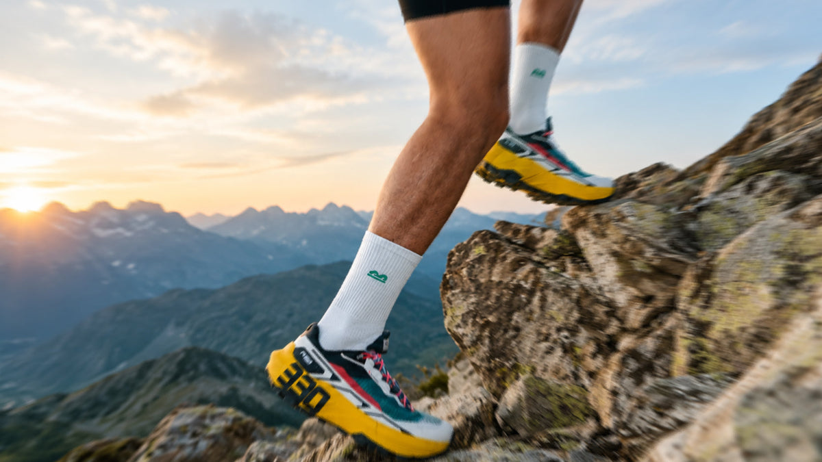 The Sock Street sports socks worn by a trail runner navigating rocky mountain terrain at sunrise
